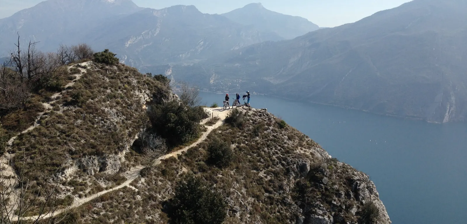 Tre biker sulla cresta sopra il lago di Garda, con le montagne del Trentino all'orizzonte